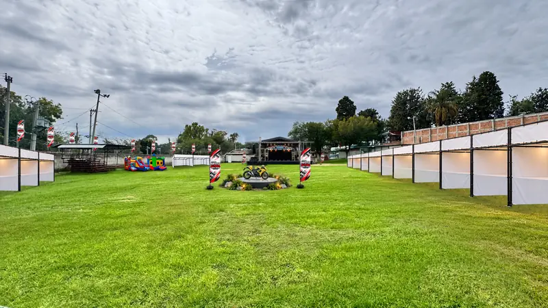 Filas de stands blancos a los lados de la cancha de pasto, con el escenario al fondo